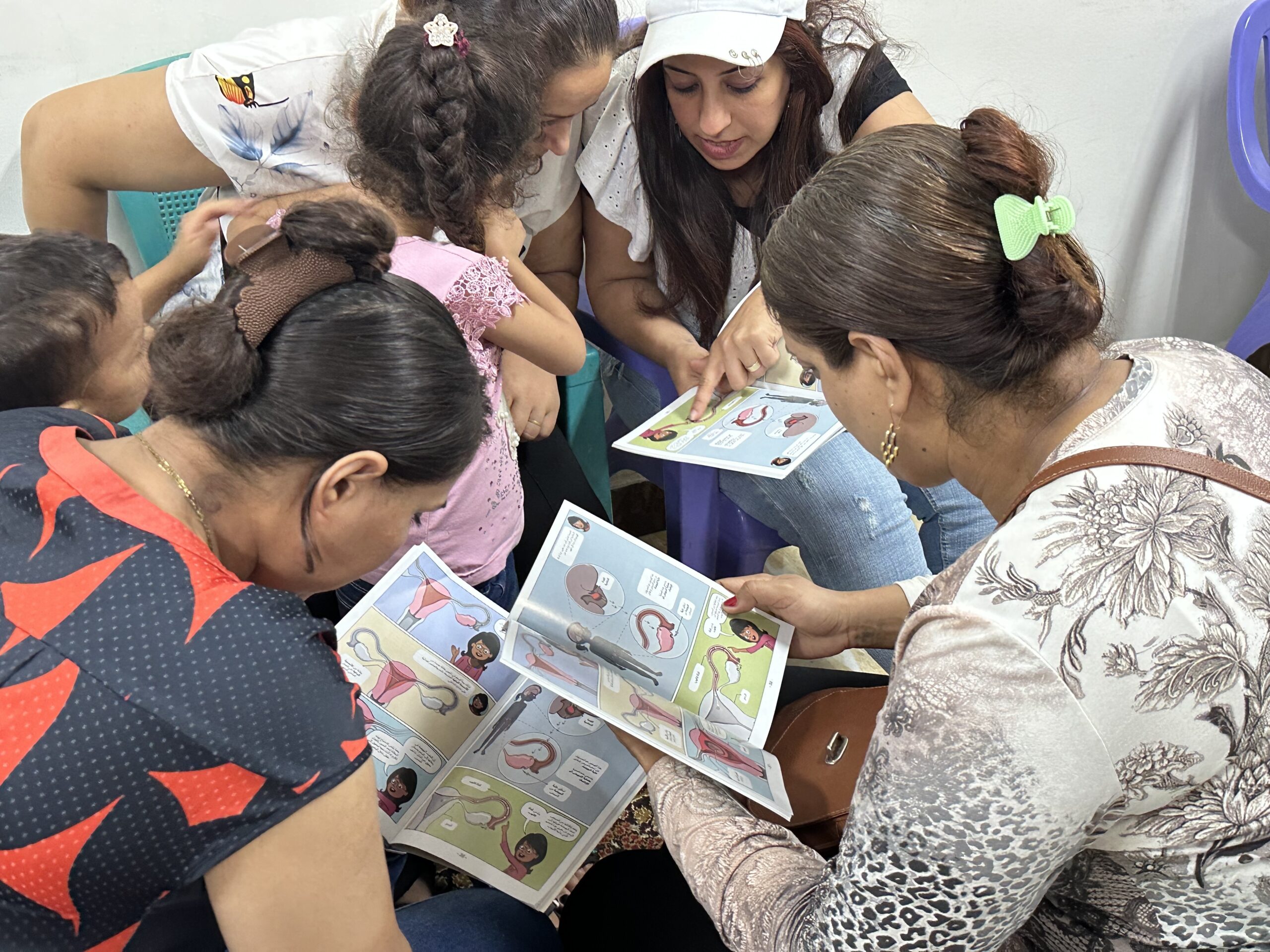 Women reviewing illustrated reproductive health booklets together in a small group setting.